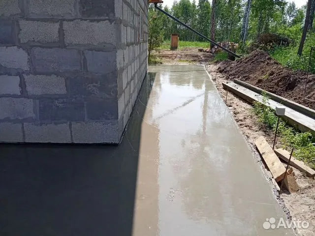 Свежезалитая бетонная отмостка вдоль стены дома из блоков